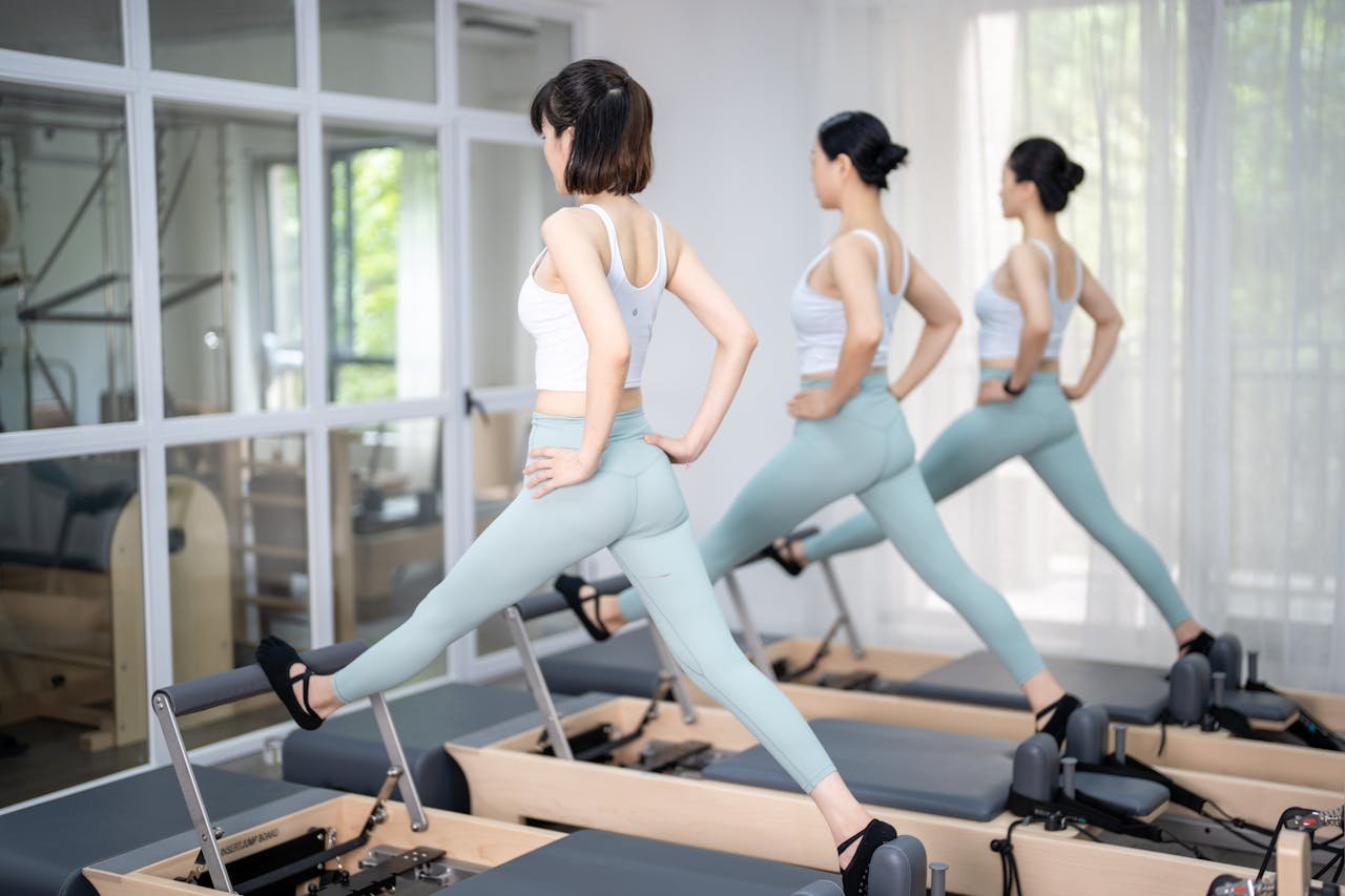 creative Three women in athletic wear exercising on Pilates reformers indoors, promoting a healthy lifestyle.