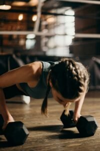 Services Fit woman doing push-ups with dumbbells indoors, emphasizing strength training and fitness.